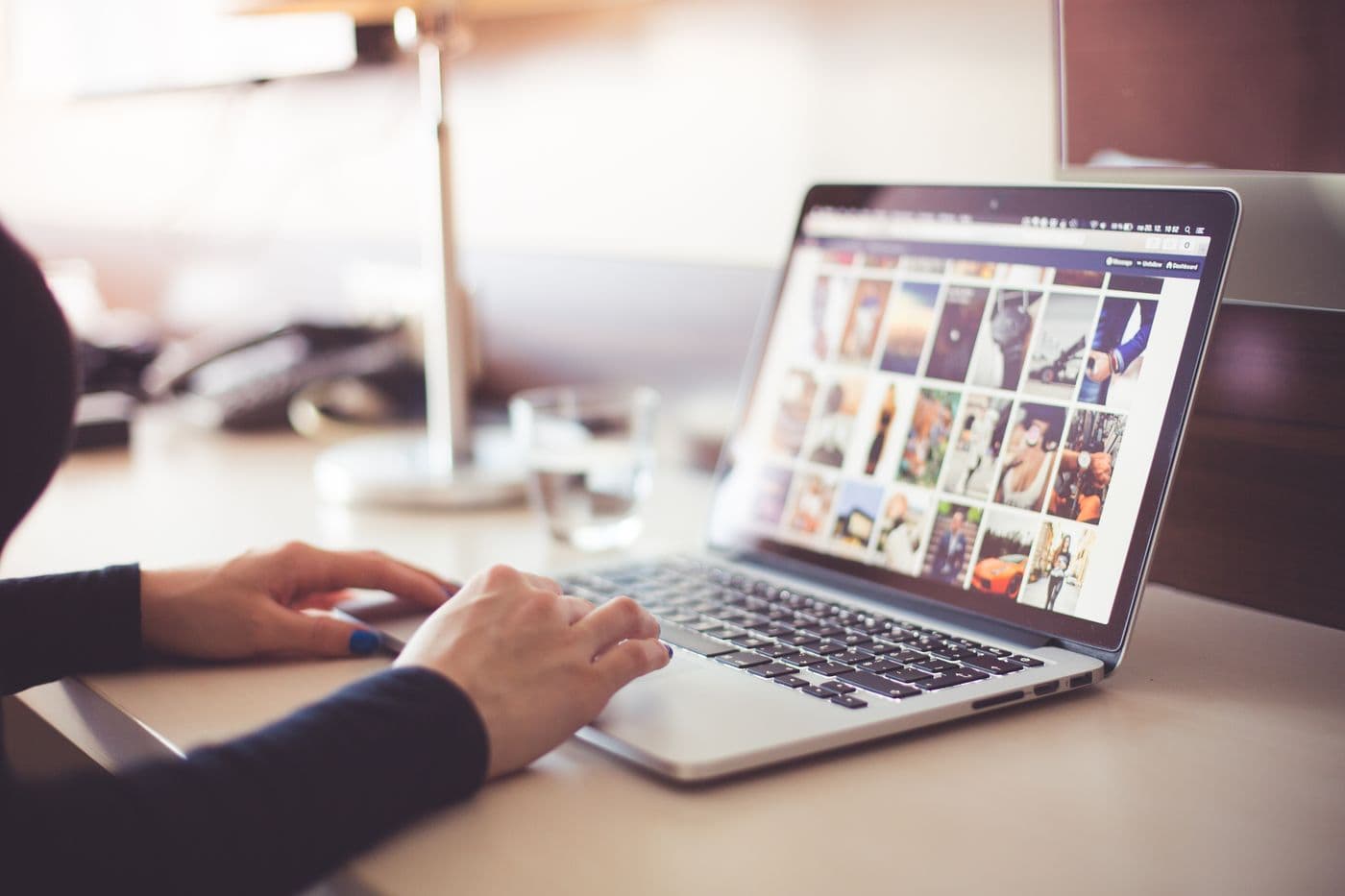 Tangan mengetik di keyboard laptop dengan layar menampilkan galeri banyak foto berukuran kecil