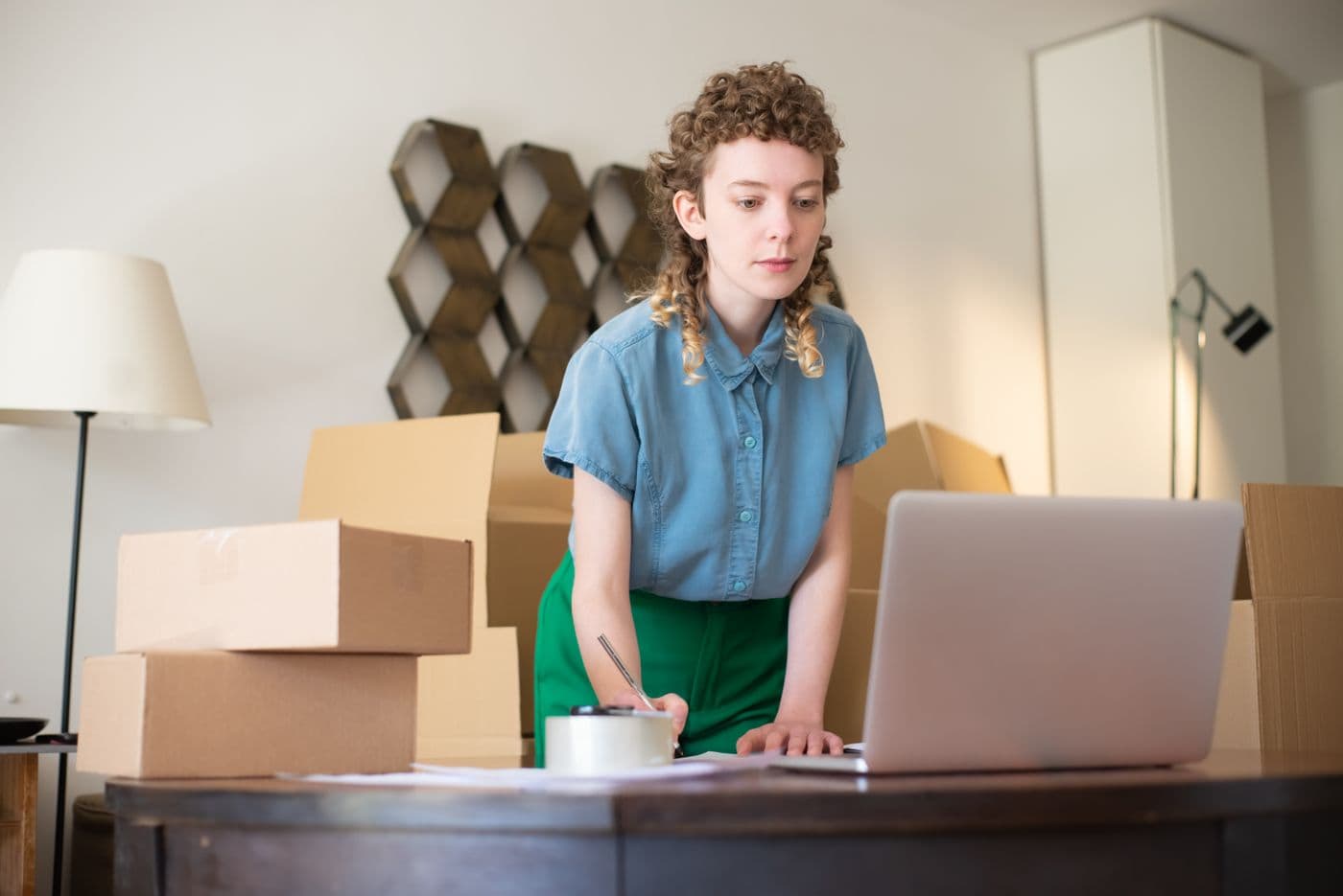 Penjual online memeriksa laptop sambil menyiapkan paket di antara tumpukan kardus