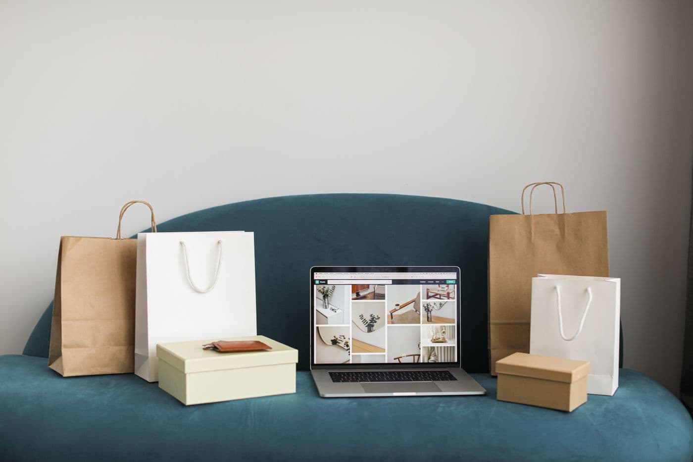 Laptop menampilkan galeri foto di atas sofa, dikelilingi tas belanja kertas dan kotak kemasan