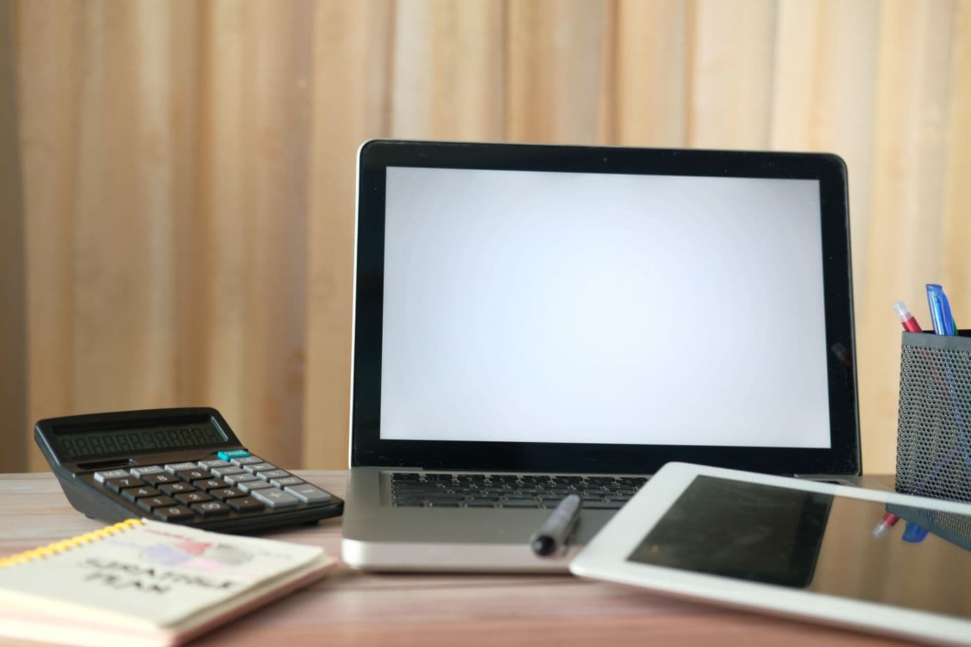 Kalkulator, laptop, tablet, dan buku catatan di atas meja kerja kayu
