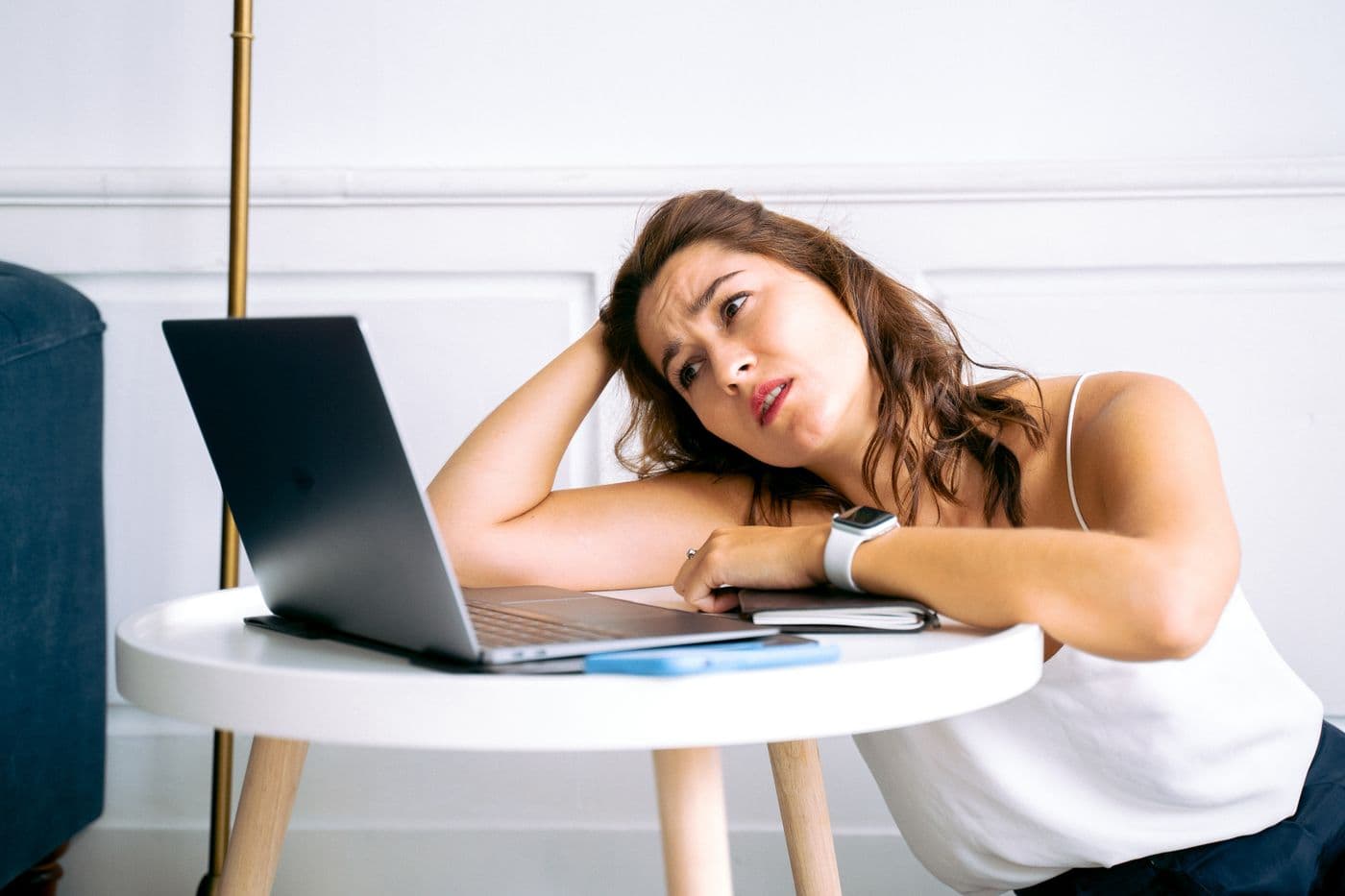 Perempuan bersandar lesu di meja sambil memegang kepala dan menatap layar laptop dengan raut bingung